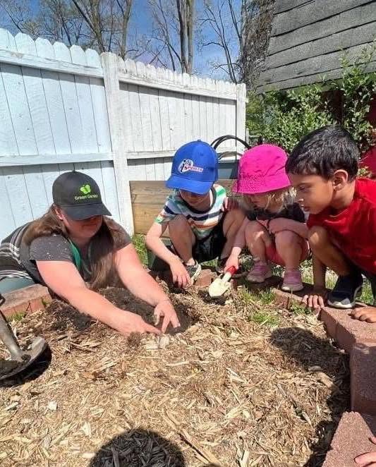 Teacher and children closely investigating the ground in an outdoor garden area