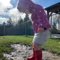 Child in red boots looking down at a puddle outdoors
