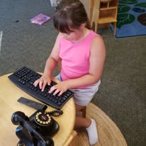 Child exploring a keyboard and a vintage telephone in a classroom