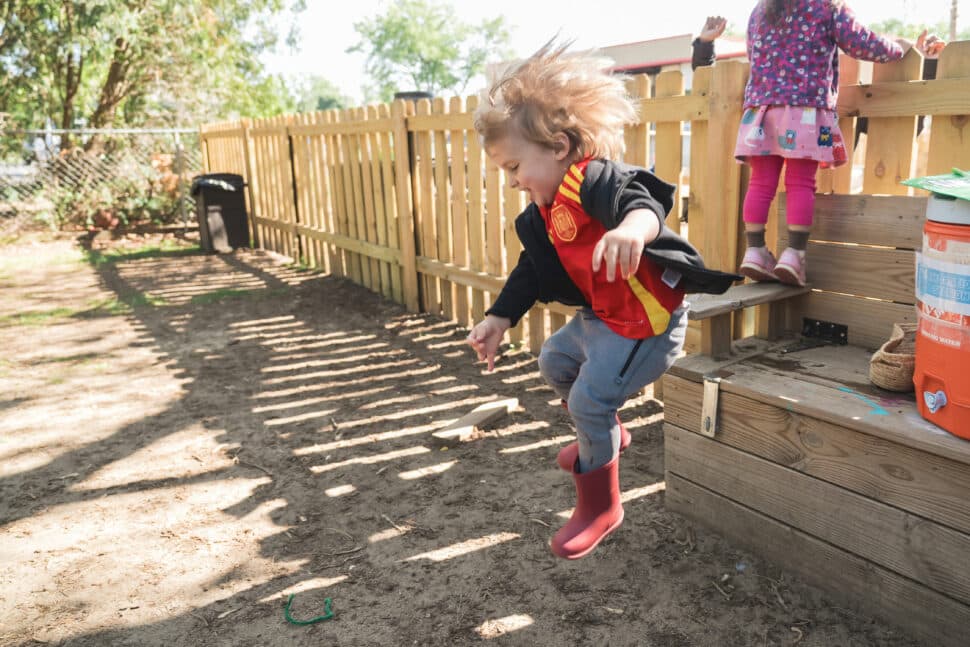 Child jumping from a wooden platform in Green Garden Clawson’s outdoor classroom