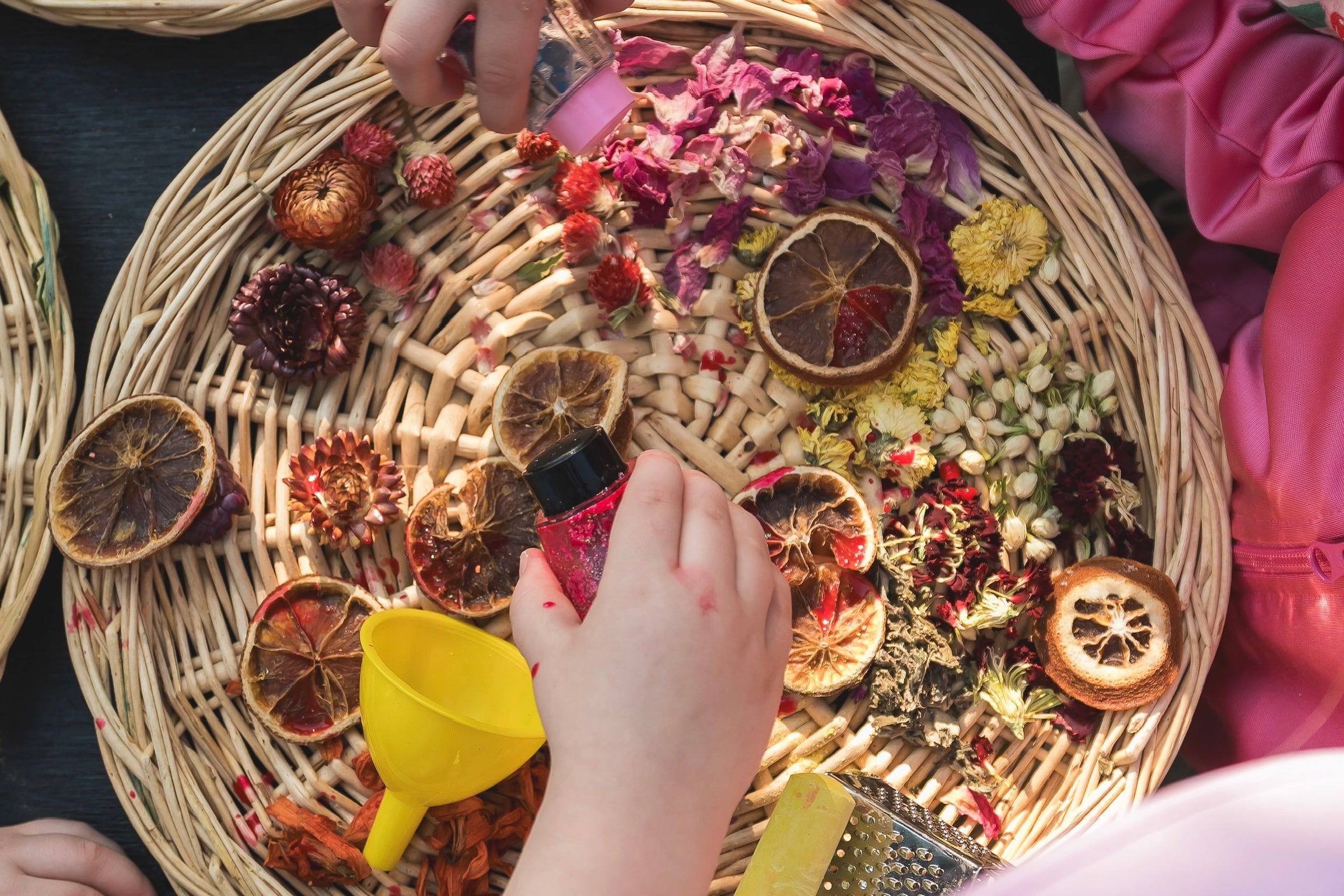 A child's hands exploring flowers and natural materials in a basket