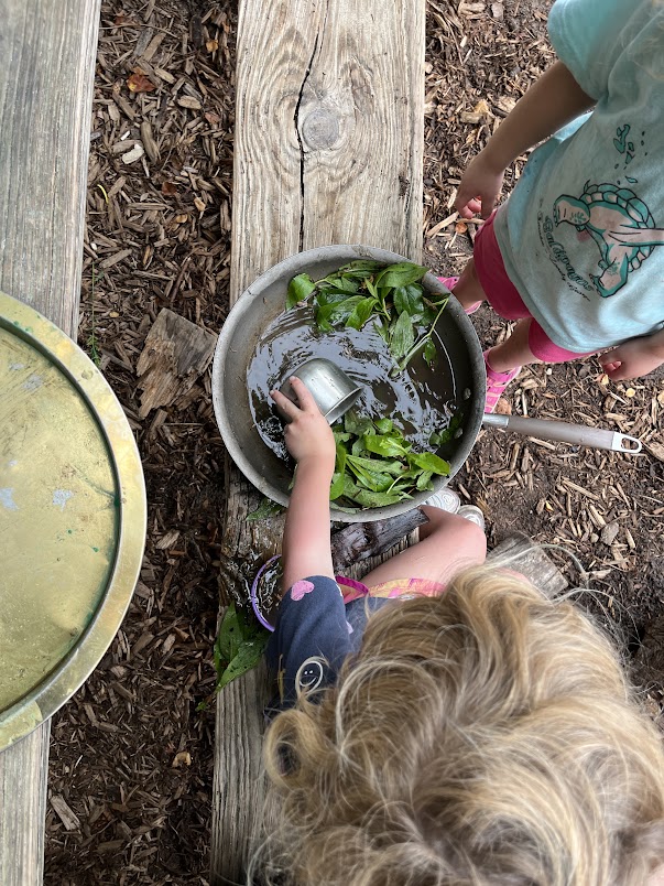 Two children mixing water and leaves in an outdoor play area