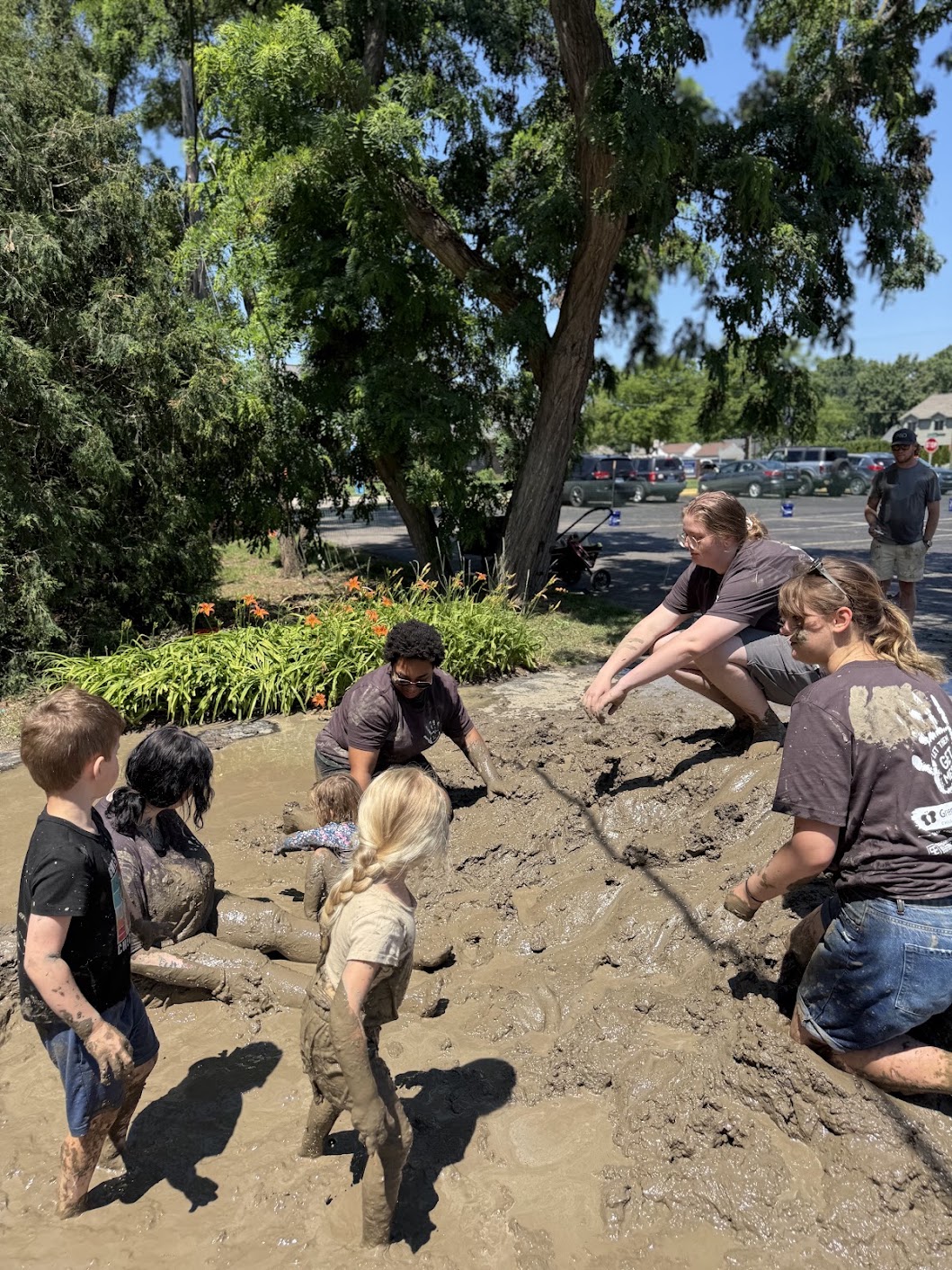 Children and adults playing together in a large muddy area on Mud Day